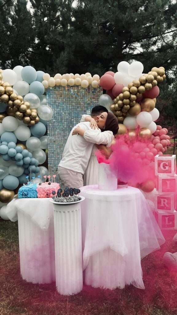 pexels-photo-18272984-18272984 Outdoor gender reveal party with balloons and cake, featuring a couple embracing joyfully.