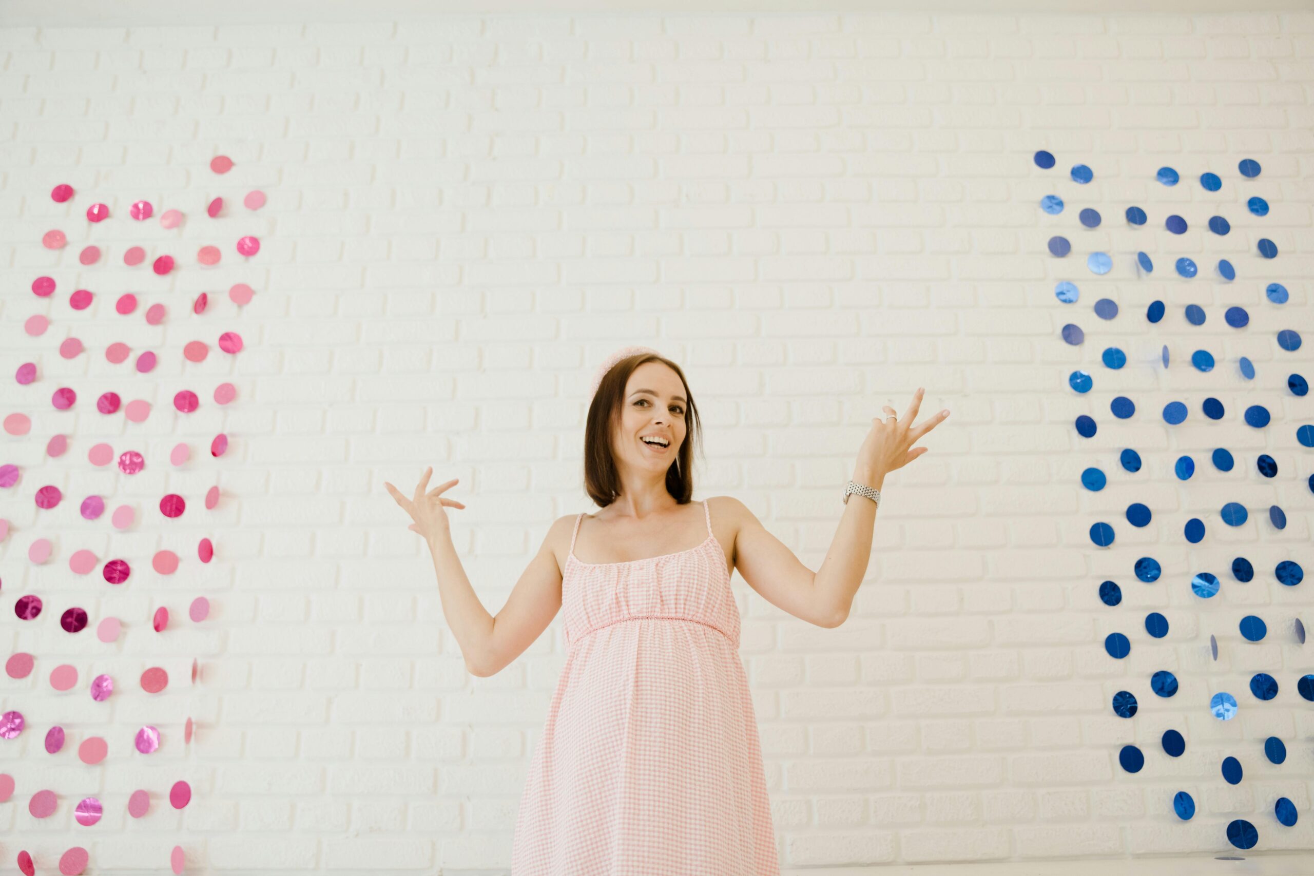 A happy pregnant woman stands between pink and blue decorations at a gender reveal party.