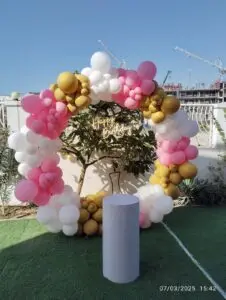 Outdoor balloon decoration in pink, white, and gold colors.